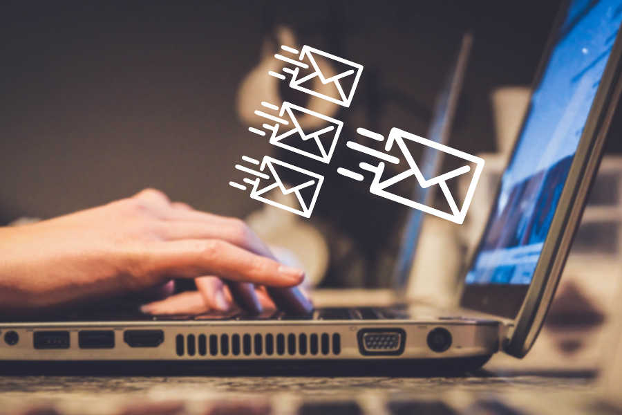 Side view of hands typing on laptop with three small and one large email icon next to the screen