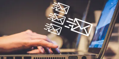 Side view of hands typing on laptop with three small and one large email icon next to the screen