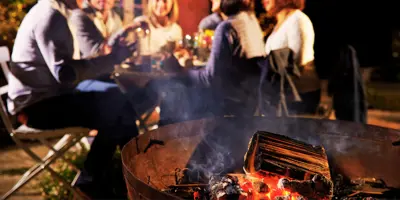 Small firepit burning in foreground with people sitting around patio table in the background having dinner