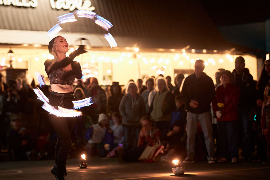 Woman spinning fire sticks in front of large crowd at night