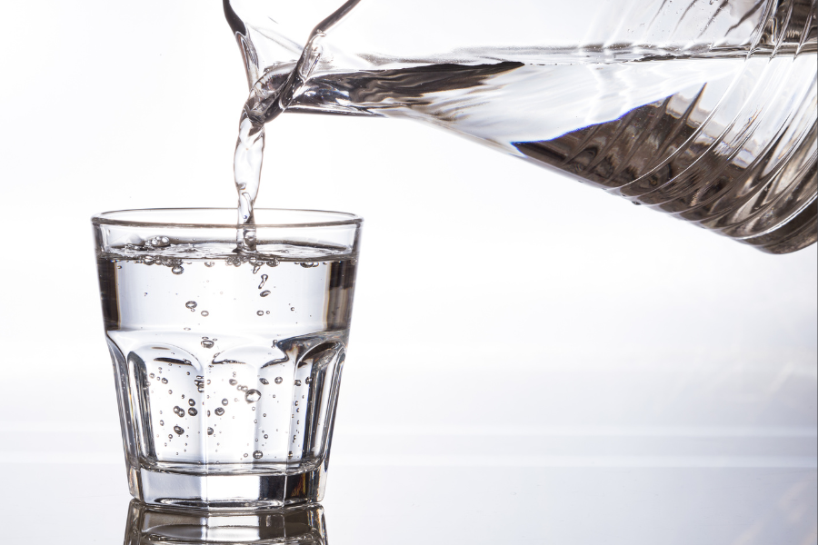 Water being poured from a clear jug into a clear glass on a white background